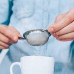 Close-up female’s hands thoroughly and accurately sifts flour